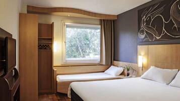 Una habitación de hotel con cama, mesita de noche, lámpara y ventana con cortinas.