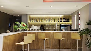 A modern bar area with a wooden counter, three bar stools, and a variety of bottles and glasses on shelves. - ibis Barcelona Cornella (Cornella de Llobregat)