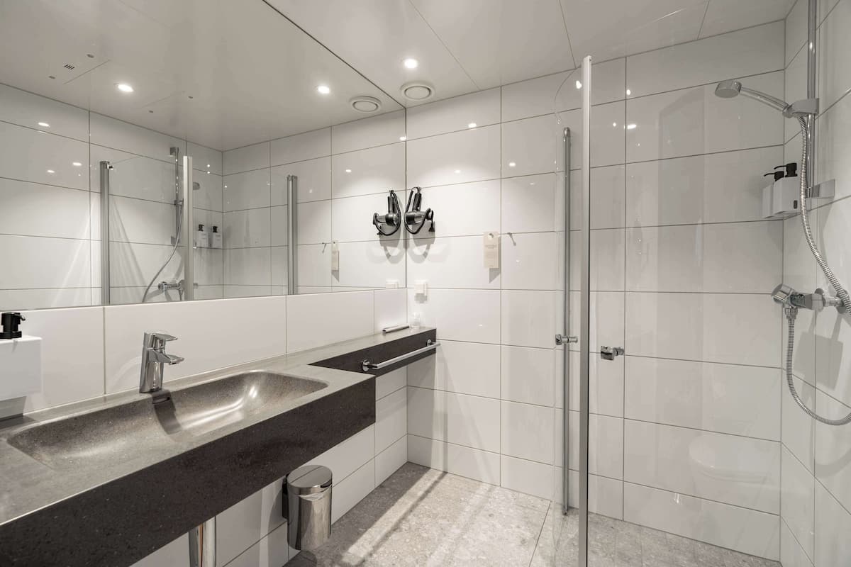 A modern bathroom with a large mirror, a double sink, and a glass-enclosed shower area.
