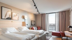 A hotel room with two beds, a sofa, a dining area, and large windows.