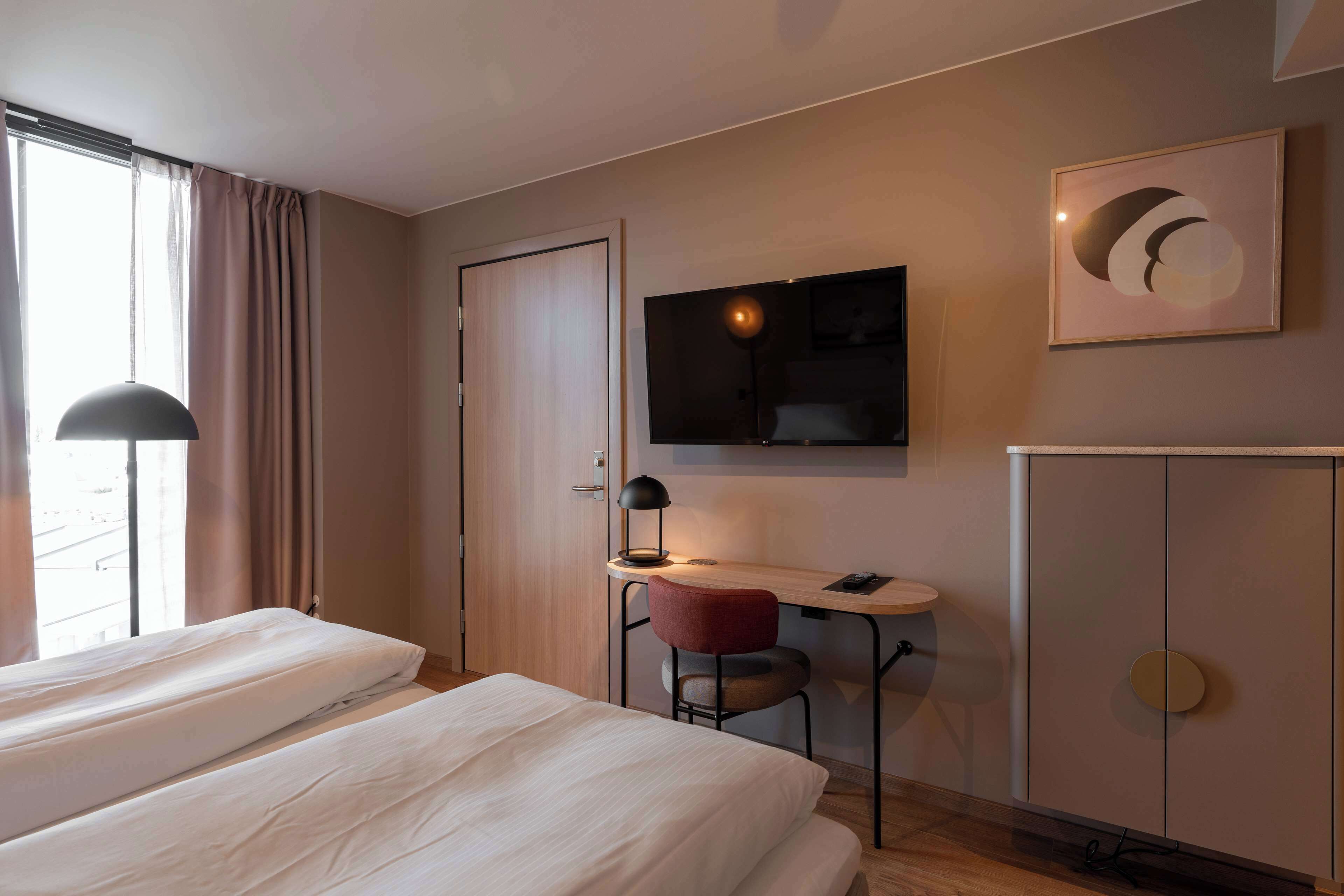 A hotel room with two beds, a desk with a chair, a TV, and a cabinet.