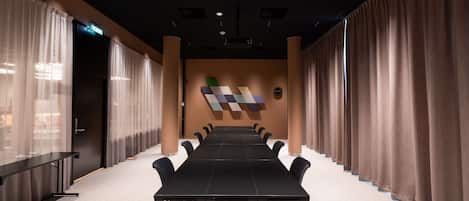 Un salón de conferencias con una larga mesa, sillas y una pantalla de proyector.