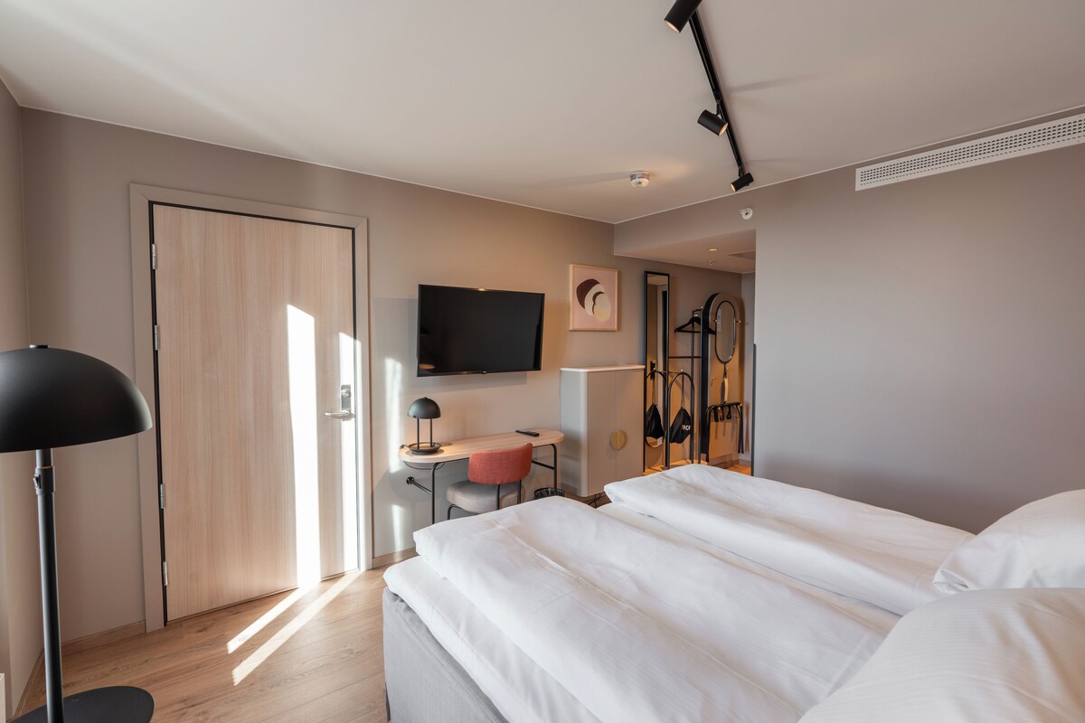 A hotel room with a bed, desk, chair, TV, and wardrobe.