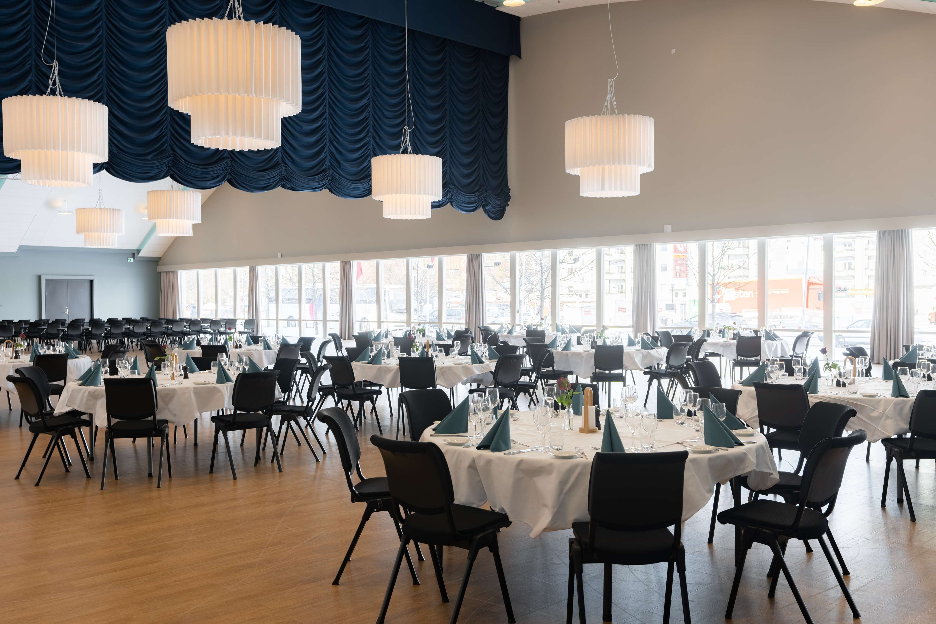 Un amplio salón de banquetes con varias mesas redondas, sillas negras y manteles blancos.