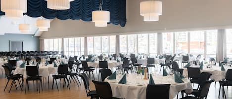 Un amplio salón de banquetes con varias mesas redondas, sillas negras y manteles blancos.