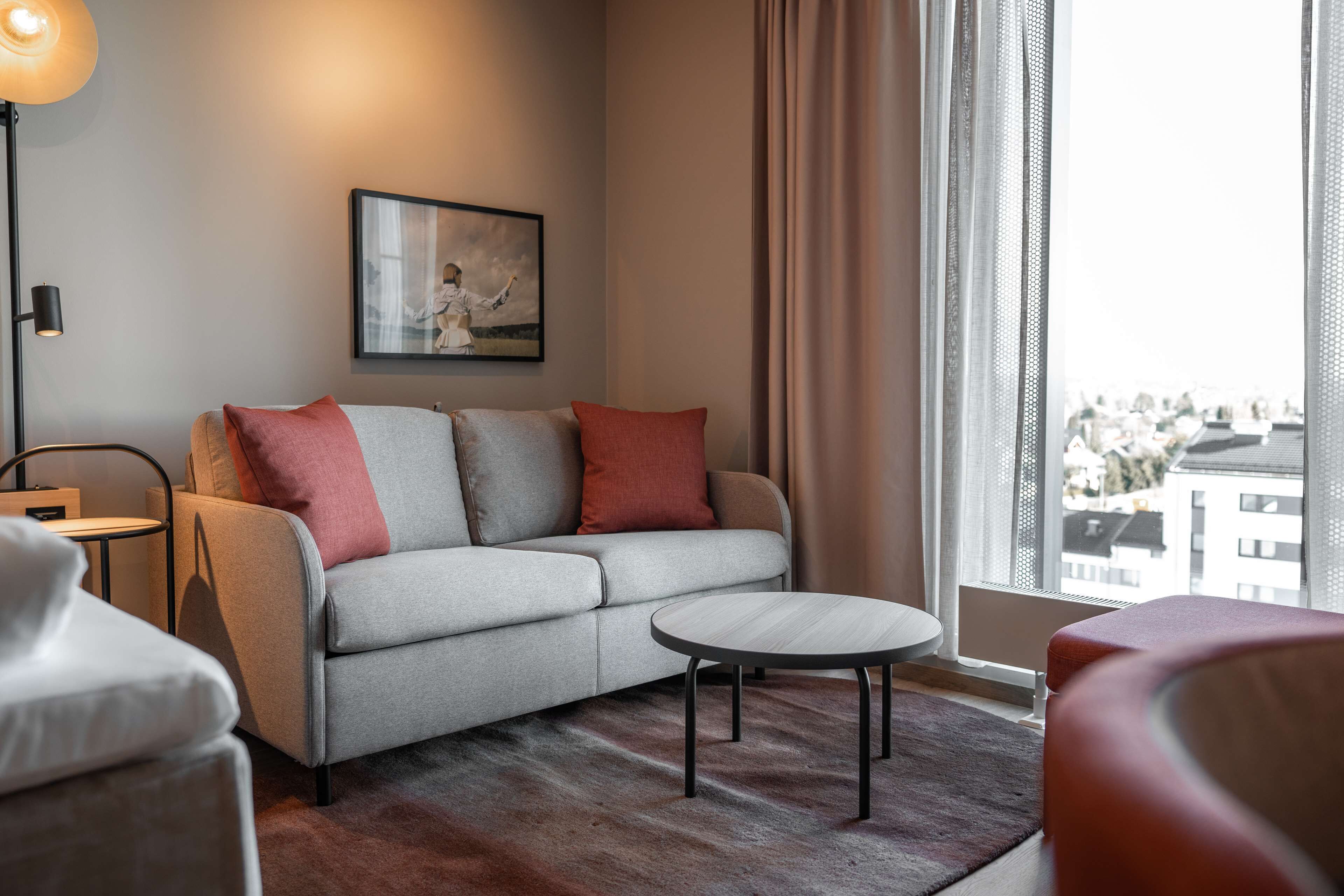 A modern living room with a grey sofa, red and grey cushions, a round coffee table, and a floor lamp.