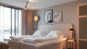 Un dormitorio moderno con una cama grande, una mesita de noche, una lámpara de pie y un ventanal con cortinas.