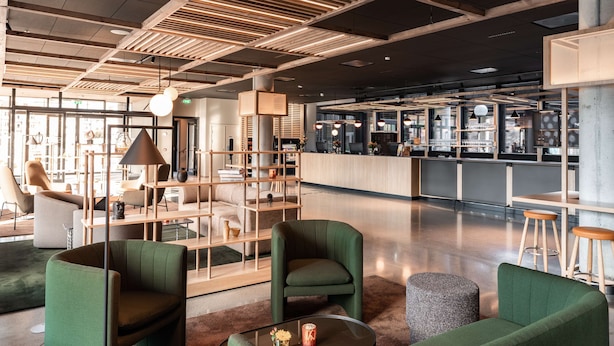 Un interior moderno con sillas tapizadas de verde, una mesa de centro de vidrio y una zona de bar con taburetes.