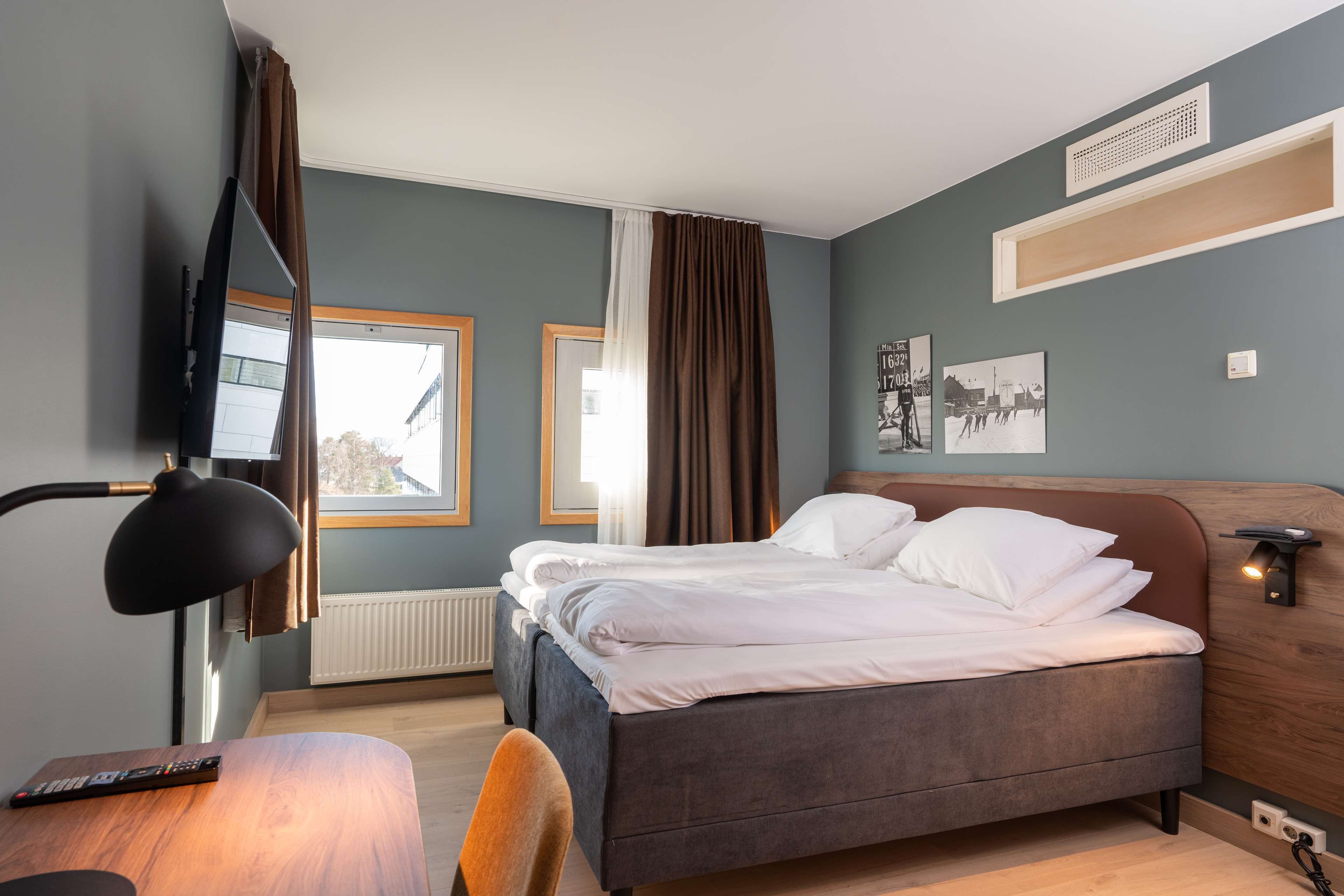 Habitación de hotel con cama, escritorio, silla, televisor y ventana con cortinas.