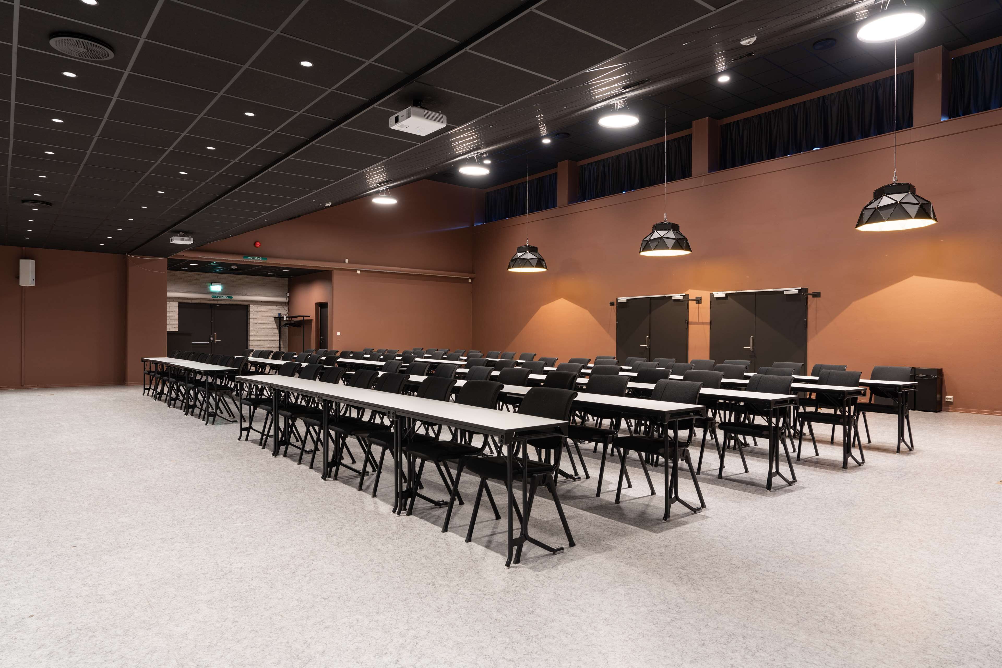A conference room with multiple tables and chairs, a projector, and a stage with curtains.