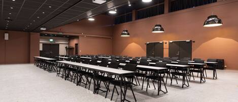 Un salón de conferencias con varias mesas y sillas, un proyector y un escenario con cortinas.
