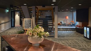 A reception area with a wooden staircase, a flower vase on a table, and a seating area with chairs and a lamp. - Scandic Luleå (Luleå)
