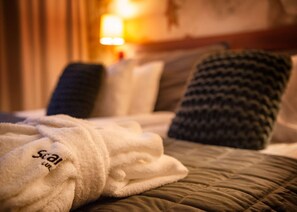 A neatly made bed with a white bathrobe on it, a brown quilted bedspread, and several pillows, including a dark patterned one.