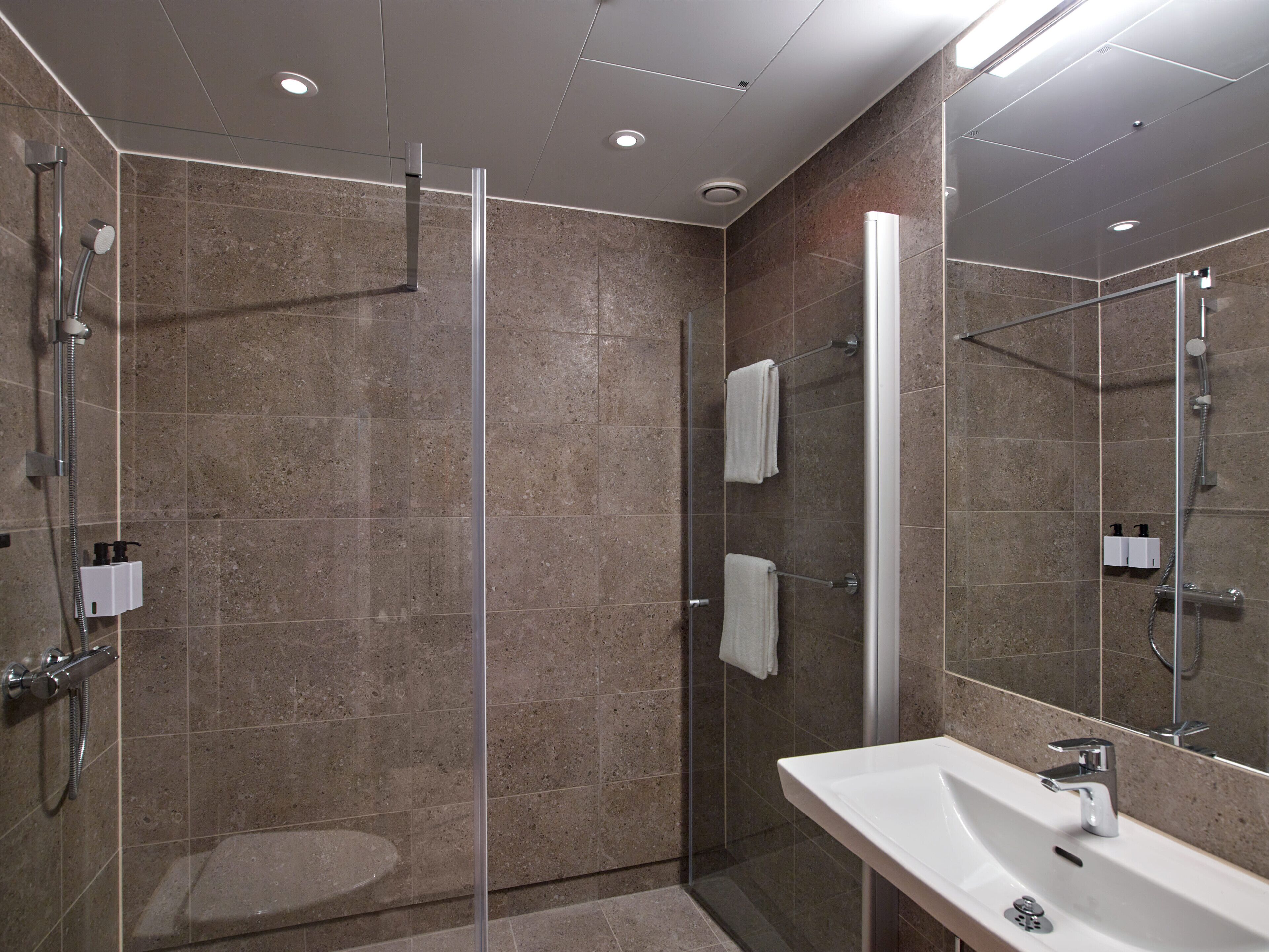 Un baño moderno con ducha envuelta en vidrio, un lavamanos blanco y un espejo grande.