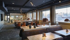 A modern restaurant interior with high ceilings, pendant lighting, and large windows offering a view of a snowy landscape. - Scandic Luleå (Luleå)