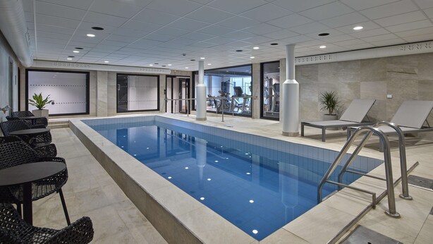 An indoor swimming pool with a tiled floor, lounge chairs, and a seating area with tables. - Scandic Luleå (Luleå)