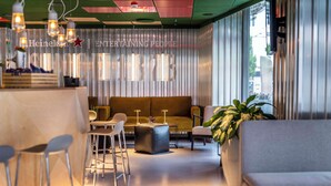 A modern lounge area with a sofa, bar stools, and a large potted plant.