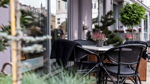 An outdoor seating area with wicker chairs and a table, surrounded by glass walls and potted plants.
