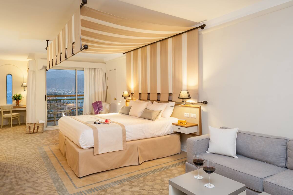 Ein Hotelzimmer mit einem großen Bett, einer Couch, einem Schreibtisch und einem Balkon mit Blick auf die Stadt.