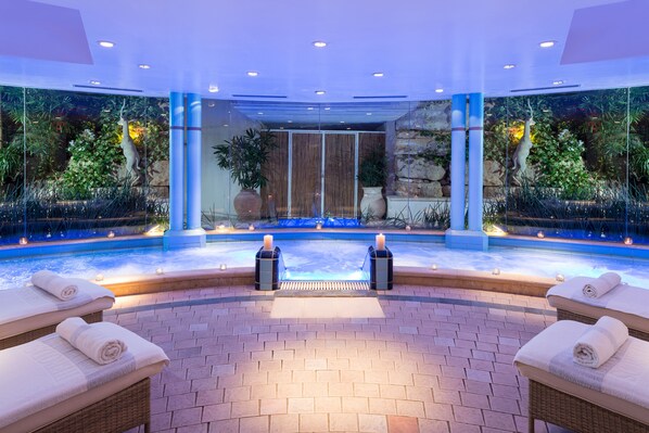 Uma área de spa com hidromassagem, duas cadeiras de massagem e uma parede decorativa com plantas e cascata.