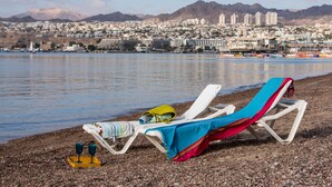 Una playa con dos tumbonas, una con una toalla de colores y una bandeja amarilla con dos vasos.