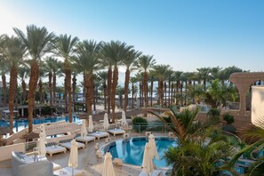 A resort pool area with palm trees, lounge chairs, and umbrellas. - Herods Vitalis Spa Hotel Eilat (Eilat)