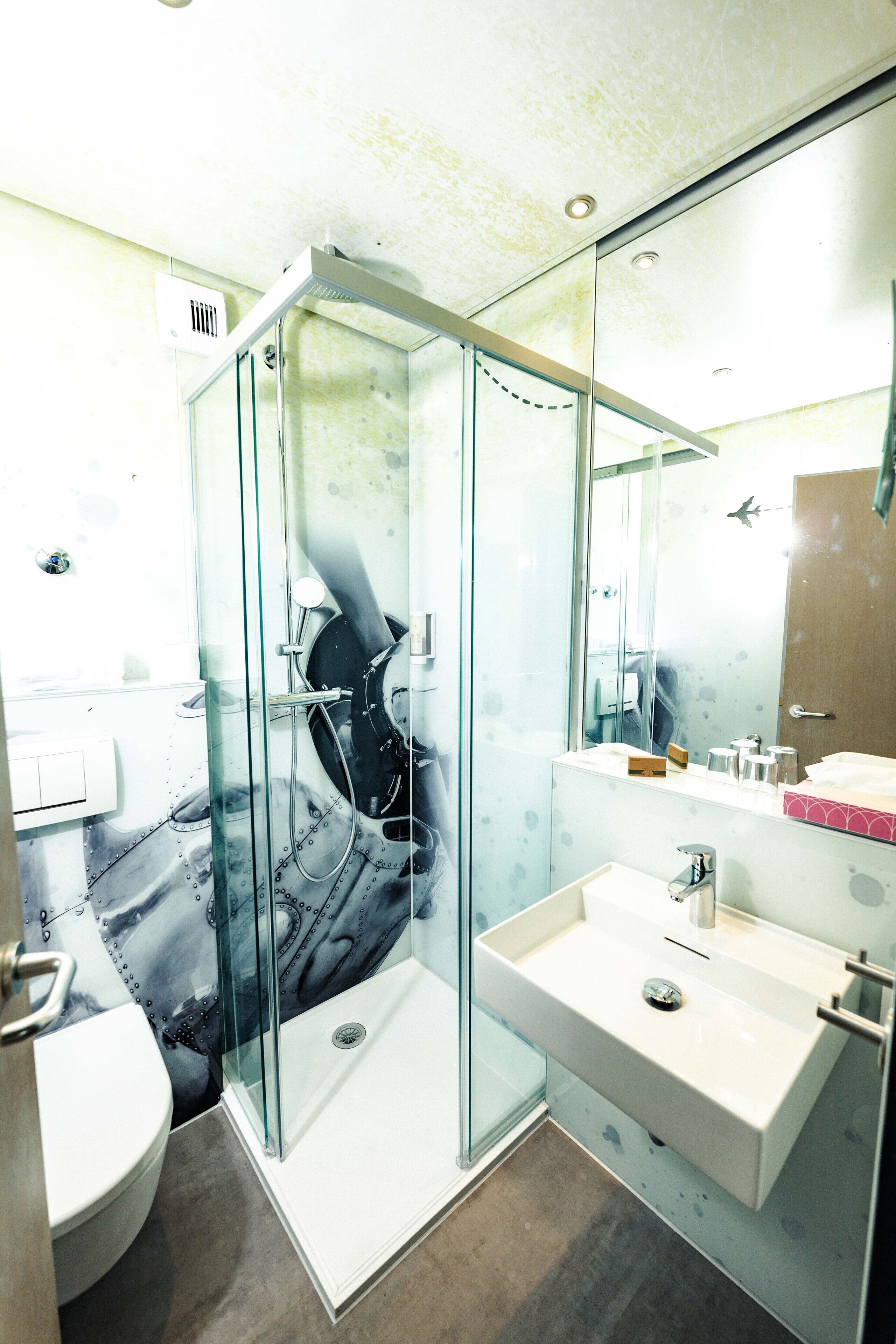 Ein modernes Badezimmer mit einer Duschkabine aus Glas, einem weißen Waschbecken und einem Spiegel darüber.