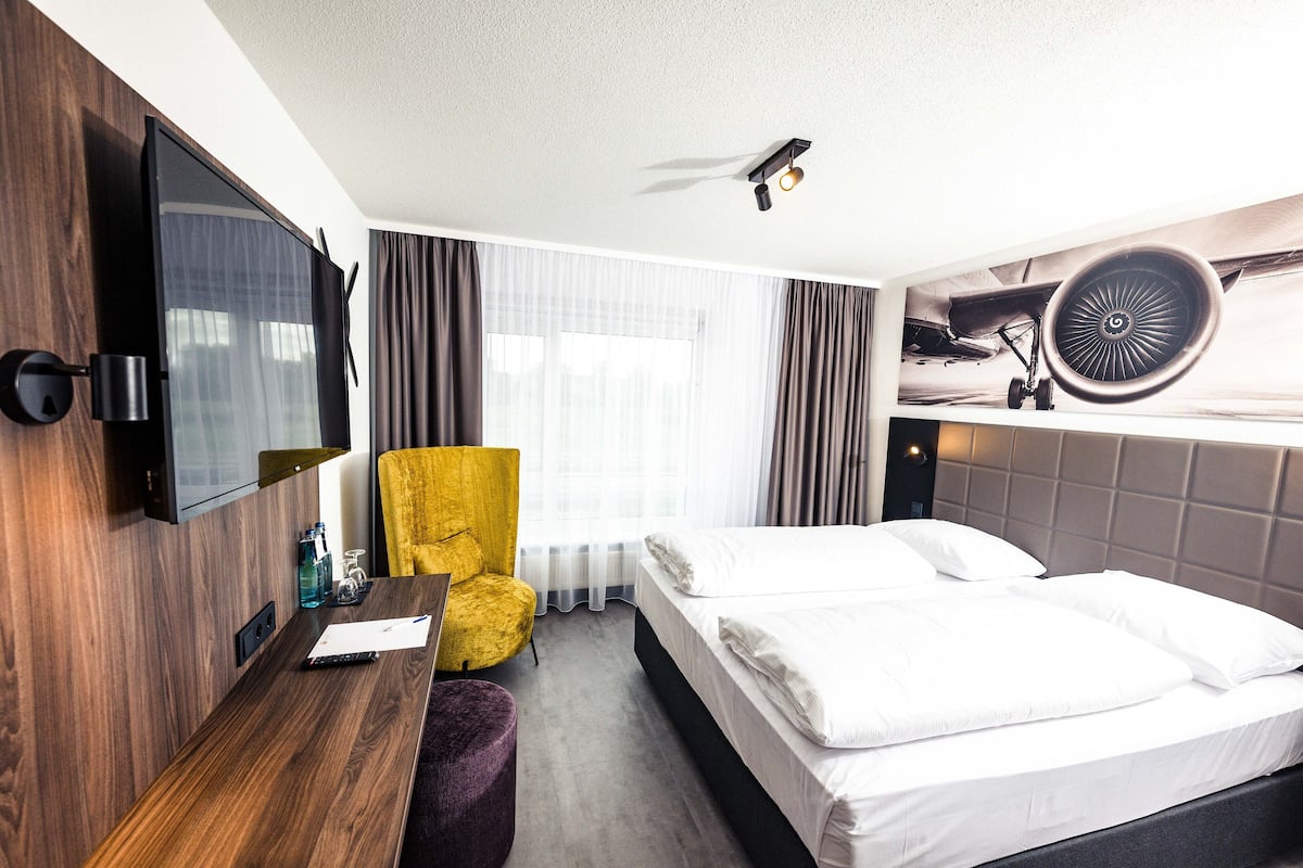 A hotel room with a bed, a desk, a chair, a TV, and a window with curtains.