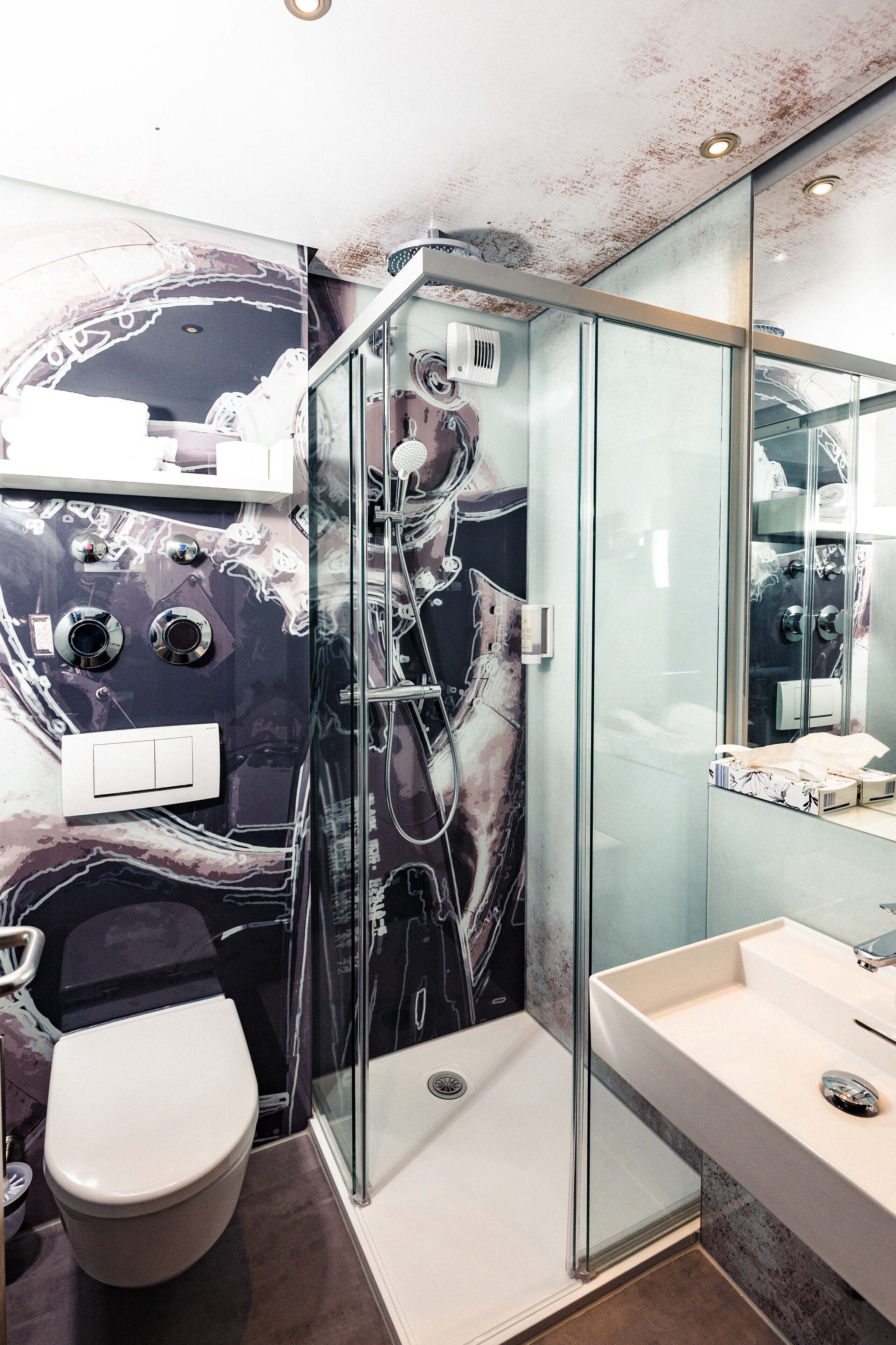 A modern bathroom with a glass-enclosed shower, a white sink, and a marble-patterned wall.