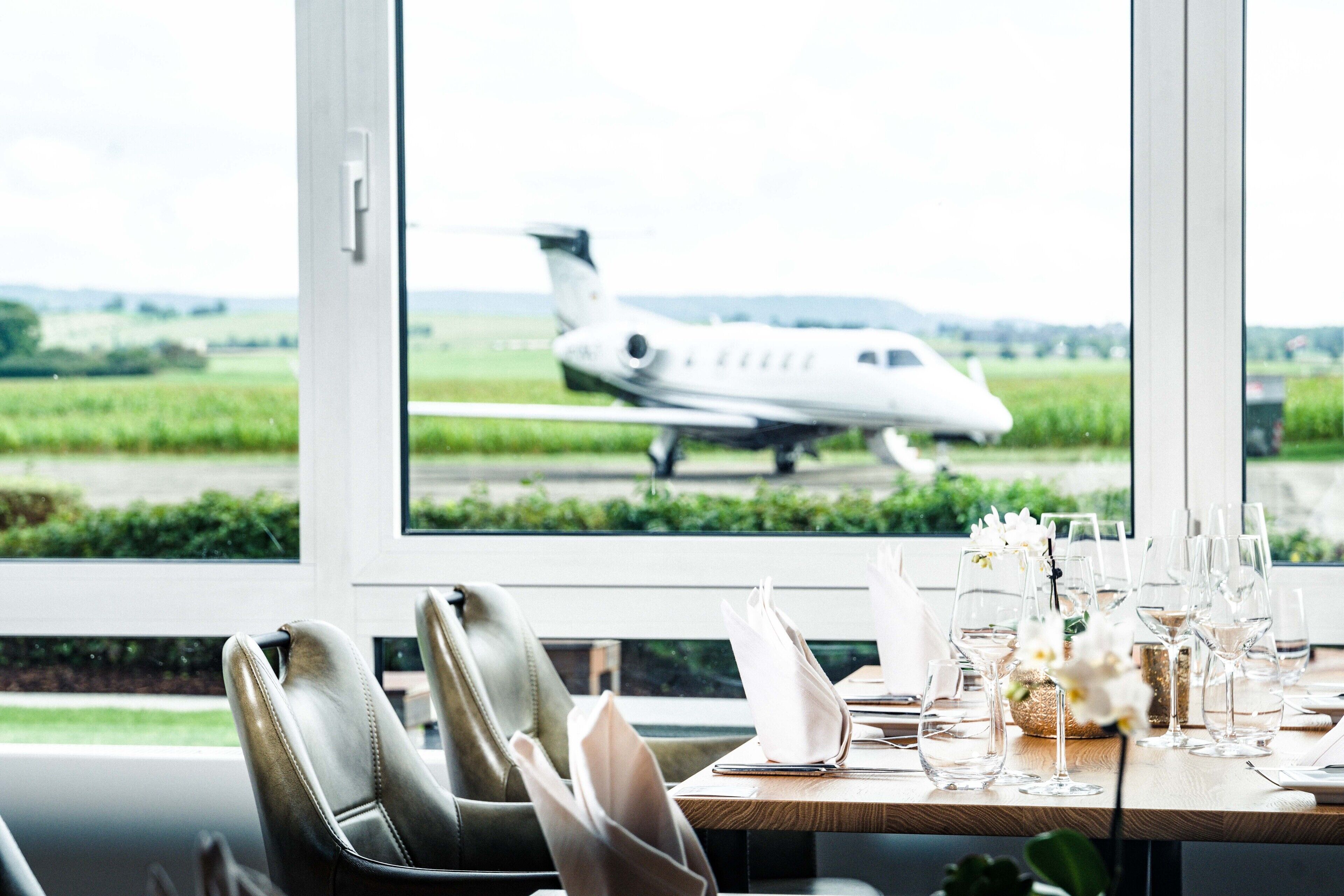 Un área de comedor con vistas a un jet privado en la pista a través de un ventanal grande.