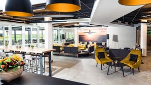 A modern lounge area with high ceilings, large windows, and a view of an airplane taking off. - Sombea Donaueschingen (Donaueschingen)