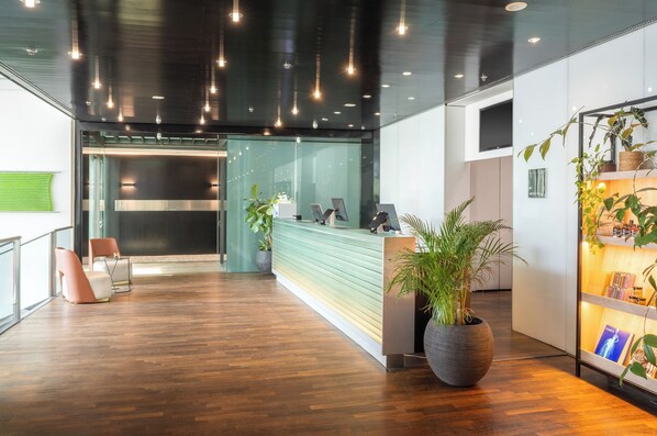 Una zona de recepción moderna con suelo de madera, un mostrador de recepción y varias plantas en macetas.