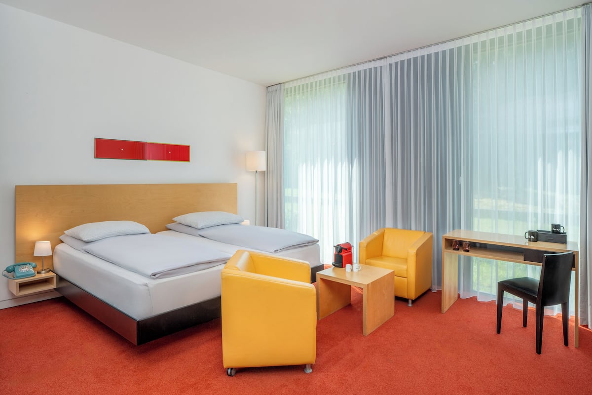Une chambre d’hôtel avec deux lits, un bureau, une chaise, une petite table et un téléphone sur la table de chevet.