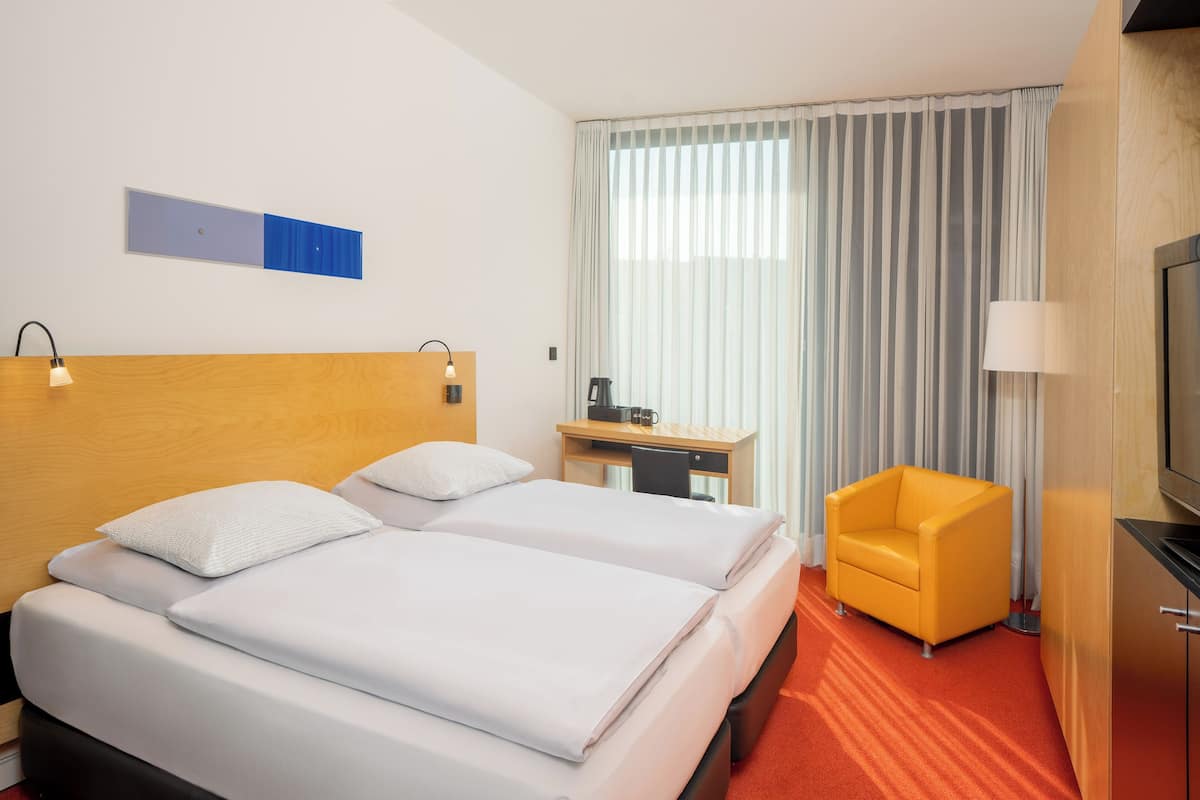 Une chambre d’hôtel avec deux lits, un bureau, une chaise et un téléviseur.