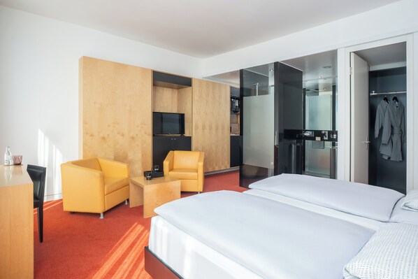 A modern hotel room with a large bed, a sofa, a desk, and a TV. - INNSiDE by Meliá Düsseldorf Seestern (Düsseldorf)