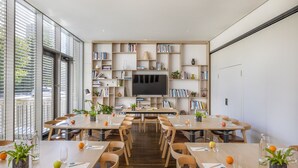 Een moderne vergaderruimte met een grote televisie, meerdere tafels, stoelen en boekenkasten.