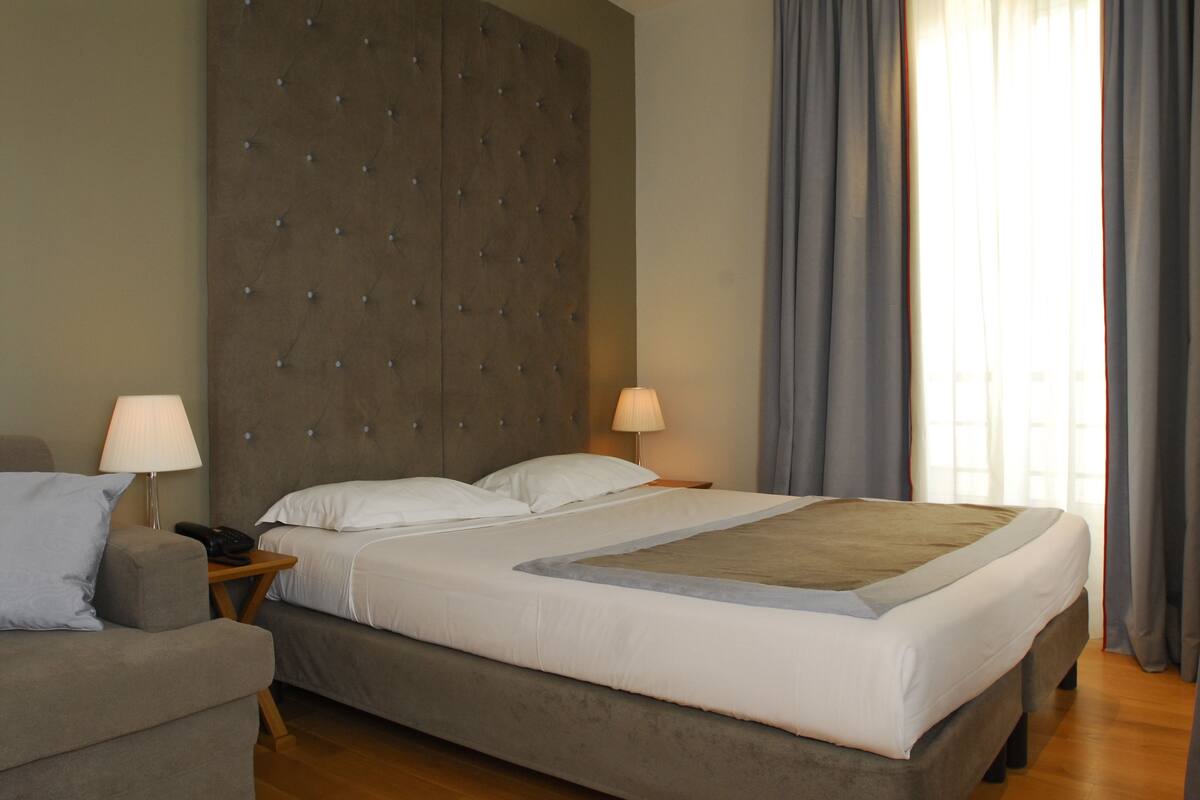A hotel room with a large bed, two bedside tables, a chair, and a headboard.