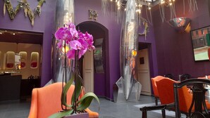 A modern interior with purple walls, a glass ceiling, and orange seating. - WHO - Windsor Hotel Opera (Paris)