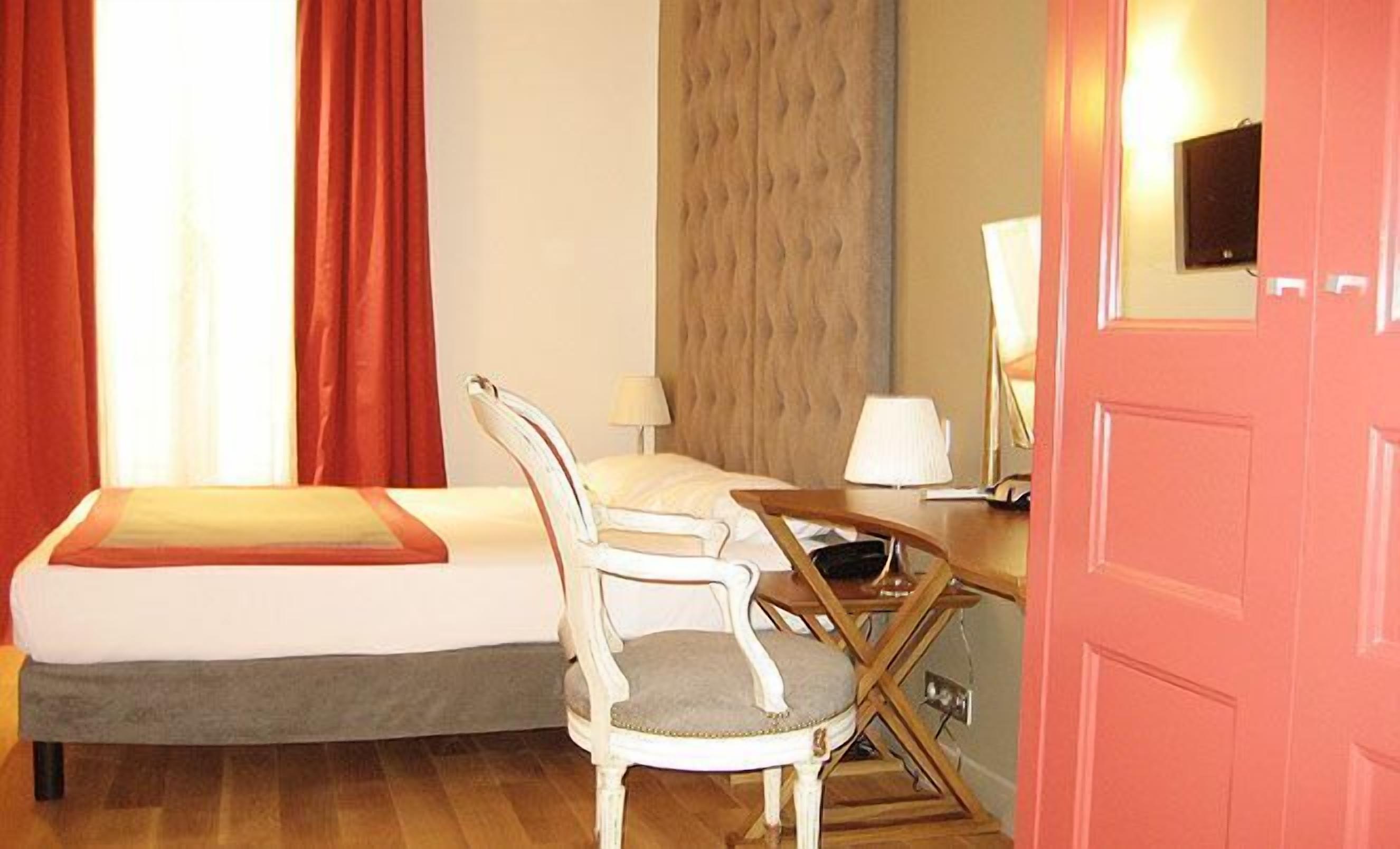 Una camera d'albergo con un letto, una sedia, una scrivania con una lampada e una televisione a parete.