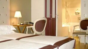 A hotel room with two beds, a desk, a chair, and a bathroom visible through an open door. - WHO - Windsor Hotel Opera (Paris)