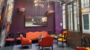 A modern interior with a purple wall, orange seating, and a television displaying the Windsor Opera. - WHO - Windsor Hotel Opera (Paris)