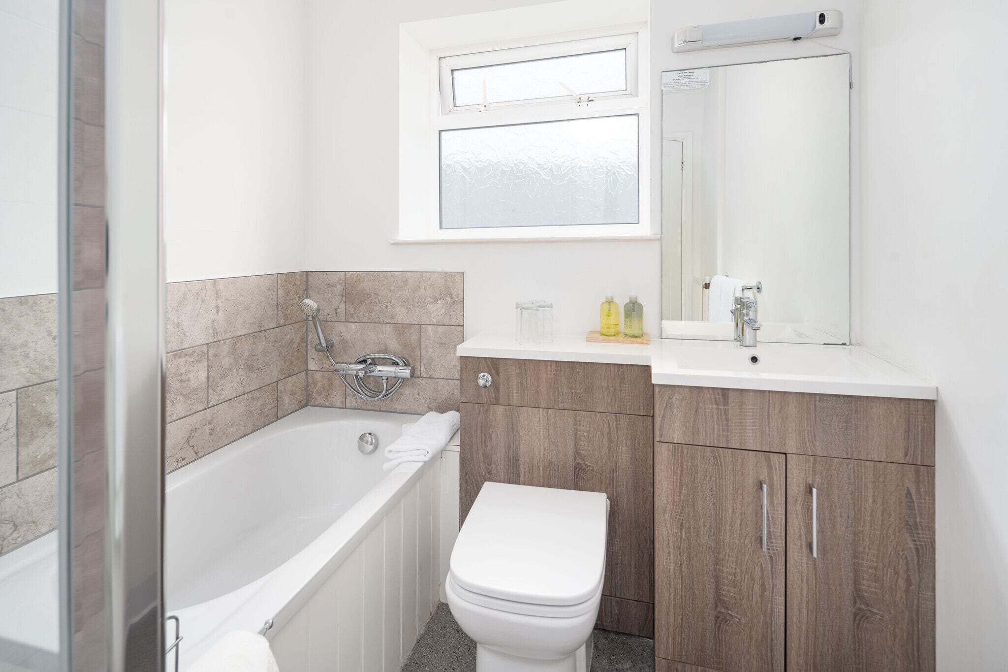 A modern bathroom with a bathtub, toilet, and vanity with a mirror.