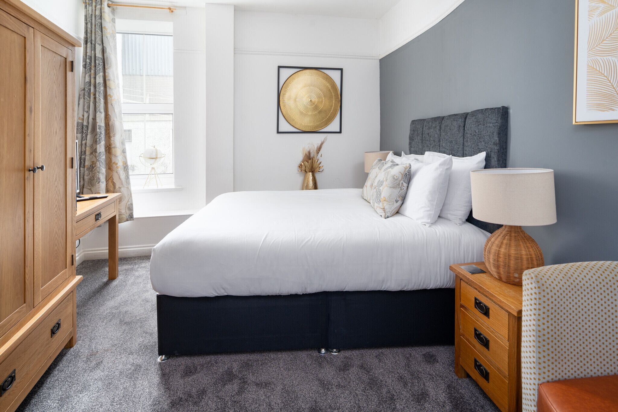 A bedroom with a bed, a nightstand, a lamp, a wardrobe, and a window with curtains.