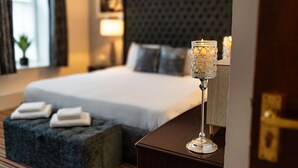 A neatly made bed with white linens, a dark upholstered headboard, and a bedside table with a glass candle holder. - Boars Head Hotel (Carmarthen)