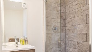 A modern bathroom with a glass-enclosed shower, a wooden vanity with a mirror, and a white sink. - Boars Head Hotel (Carmarthen)