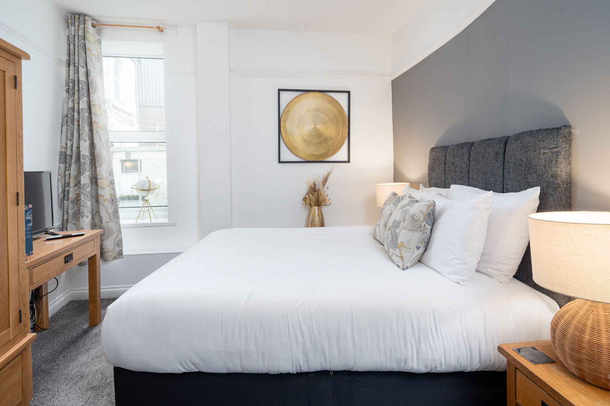 Une chambre à coucher bien rangée, avec un grand lit, une table de chevet, une lampe et une œuvre d’art encadrée accrochée au mur.