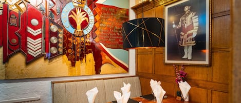 A dining area with a wooden table set for four, a decorative wall with a coat of arms, and a framed portrait.