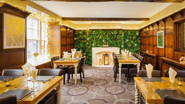 A restaurant with wooden tables and chairs, a patterned carpet, and a green wall with plants. - Boars Head Hotel (Carmarthen)