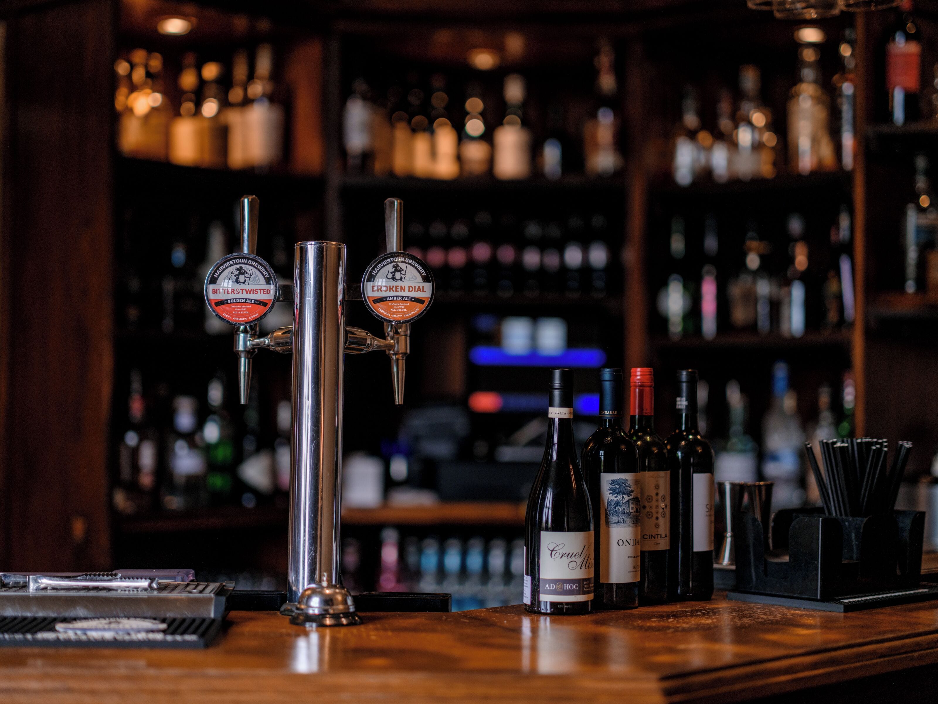 Una barra con dos grifos de cerveza identificados como 'Bit Twisted' y 'Erken Dial', una selección de botellas de vino y una herramienta de bar sobre la encimera.