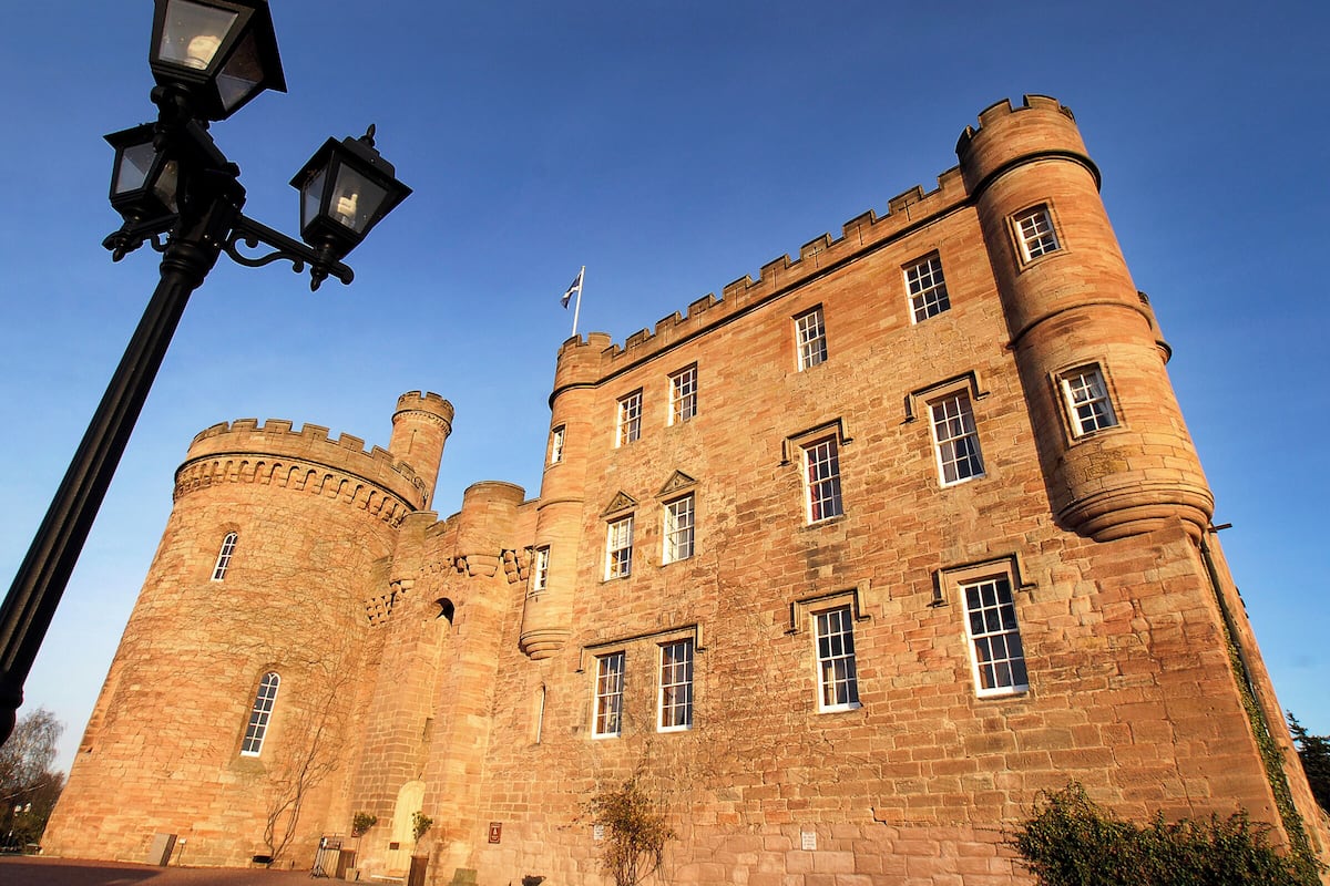A historic stone castle with multiple windows, a flag, and a street lamp.